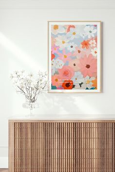 a vase with flowers sitting on top of a wooden cabinet next to a wall mounted art piece