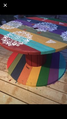 a multicolored wooden table sitting on top of a wooden deck with flowers painted on it