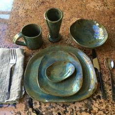 a table set for four with silverware and napkins on it, including two coffee mugs