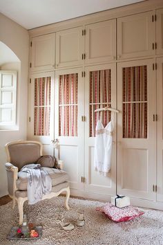 a white closet with clothes hanging on it's doors and a chair in the corner