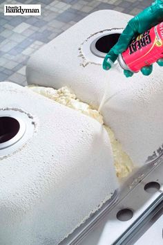 a person in green gloves is spreading cheese on a stove top with a red bottle