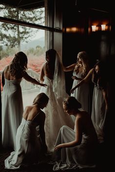 a group of women standing around each other in front of a window with their hands on the bride's dress