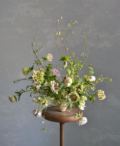 an arrangement of flowers in a vase sitting on a small table against a gray wall