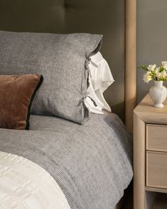 a white vase with flowers sitting on top of a bed next to a night stand