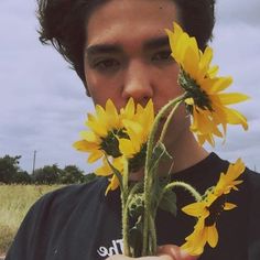 a young man holding sunflowers up to his face