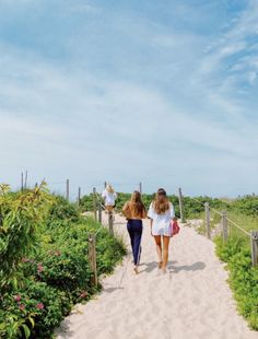 two girls walking down a path in the sand with their backs turned to the camera