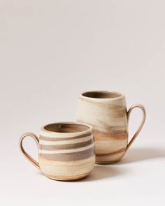 two coffee mugs sitting side by side on a white surface with no one around them