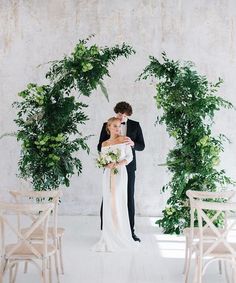 a bride and groom standing in front of an arch with greenery on the wall