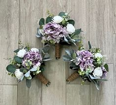 three bridal bouquets with purple and white flowers are arranged on a wood floor