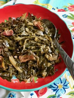 a red bowl filled with collard greens and meat on top of a floral table cloth