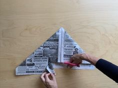 someone is cutting out newspaper from a piece of paper that has been placed on top of a wooden table