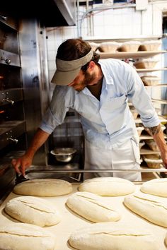 a man working in a kitchen with lots of uncooked bread on the counter