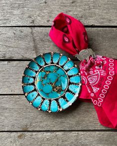 two pieces of jewelry sitting on top of a wooden table next to a red scarf