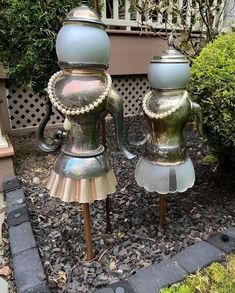 two metal vases sitting on top of each other in front of some bushes and trees