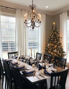 a dining room table is set for christmas with blue and white plates, silverware, and candles