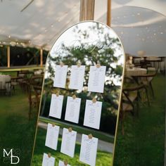 a mirror with seating cards attached to it in the middle of a grassy area under a tent