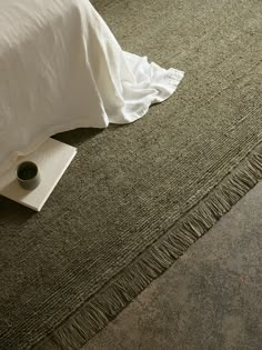 a close up of a bed with a pillow on the floor and a cup next to it