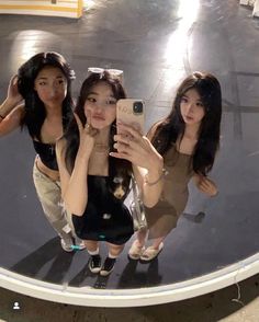 three young women taking a selfie in front of a mirror with their cell phones