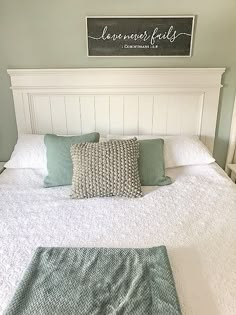 a white bed with green pillows and a sign on the wall above it that says, somewhere feels