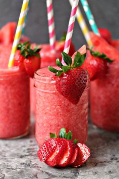 strawberry smoothie in mason jars with strawberries on the rim and two drinking straws sticking out of them