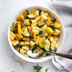 a white bowl filled with squash and zucchini on top of a table next to a cutting board