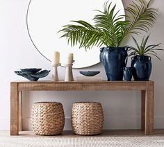 a wooden table topped with blue vases next to a mirror and two planters