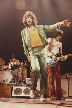 the rolling stones performing on stage with their guitars in hand and one man holding an electric guitar