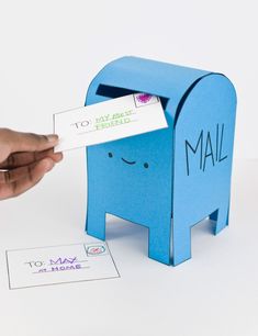 someone is holding up a small blue mailbox with a card in it's mouth