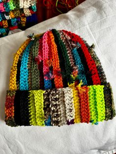 multicolored knitted hat laying on top of a white sheet next to other crocheted hats