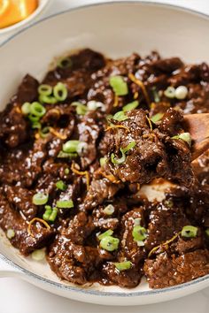 a white bowl filled with beef and green onions