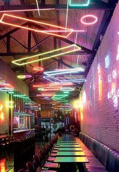 an empty restaurant with neon lights hanging from the ceiling and long tables lined up along the wall