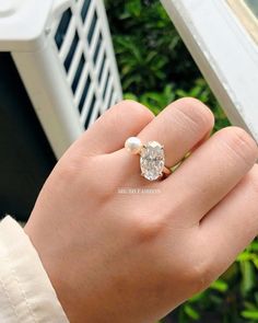 a woman's hand holding a ring with a diamond and pearl in the middle