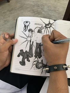 a person holding a pen and writing in a notebook with drawings on it's pages