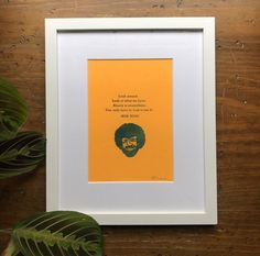 an orange and green print with a quote on it next to a plant in a white frame