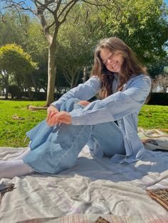 a woman sitting on top of a blanket next to a tree