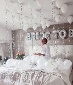 a woman sitting on top of a bed surrounded by balloons