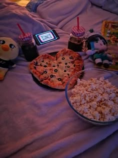 two pizzas and popcorn on a bed next to a penguin doll, an ice cream sundae