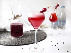 three glasses filled with different colored drinks on top of a white tablecloth and silver sequins