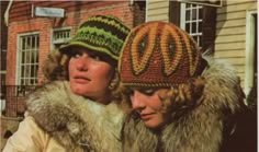 two women wearing knitted hats in front of a brick building