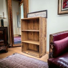 a wooden book shelf sitting on top of a hard wood floor next to a red chair