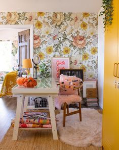 a room with a table, chair and wallpaper on the walls is decorated in bright colors