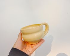 a hand holding a cream colored cup in front of a white wall with shadows on it