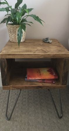 a wooden side table with a plant on top and a book next to it in front of a bed