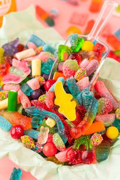 a bowl filled with lots of colorful gummy bears on top of a pink table