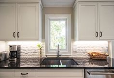 a kitchen with white cabinets and black counter tops is pictured in this image, there are two windows above the sink