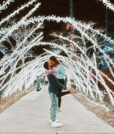 a man and woman kissing in front of christmas lights on the walkway at night time