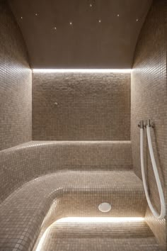 a tiled bathroom with a shower head and hand held showerhead in the corner, illuminated by recessing lights