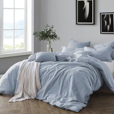 a bed with blue comforters and pillows in a white room next to a window