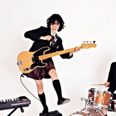 a man in a suit and tie playing an electric guitar next to a drum set