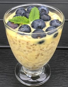 a glass bowl filled with pudding and blueberries on top of a wooden table next to a green leaf